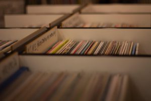 Rows of vinyl records in a record store, with dividers and handwritten labels visible, shot with a shallow depth of field.